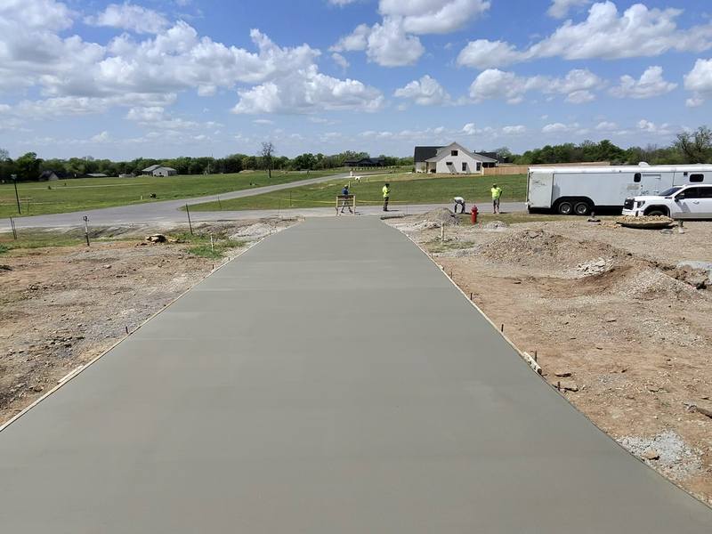Freshly finished concrete driveway stretching toward a new home under a blue Oklahoma sky