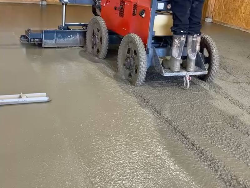 Crew member running a walk-behind power trowel across fresh concrete